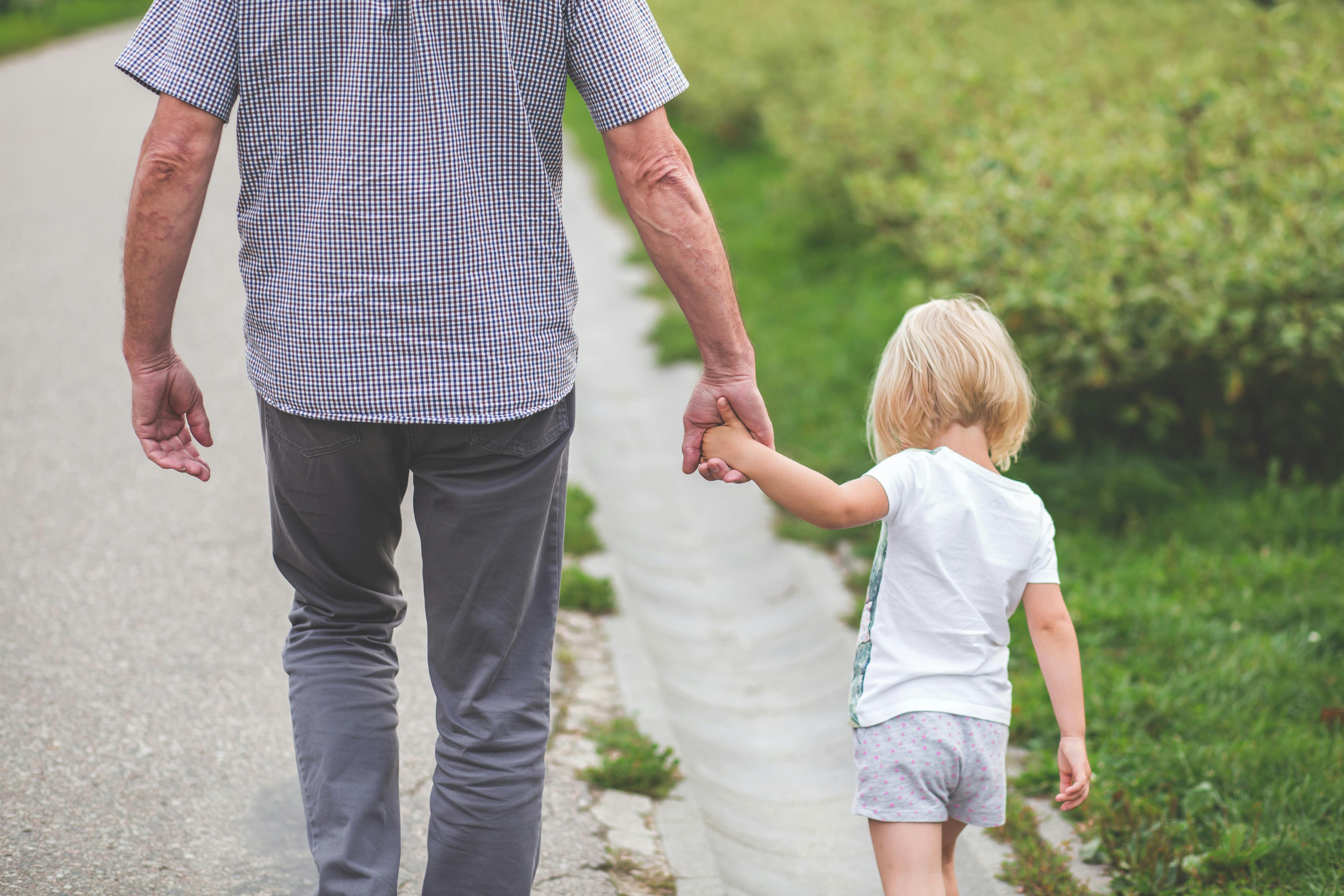 A father and his young daughter walk hand-in-hand.