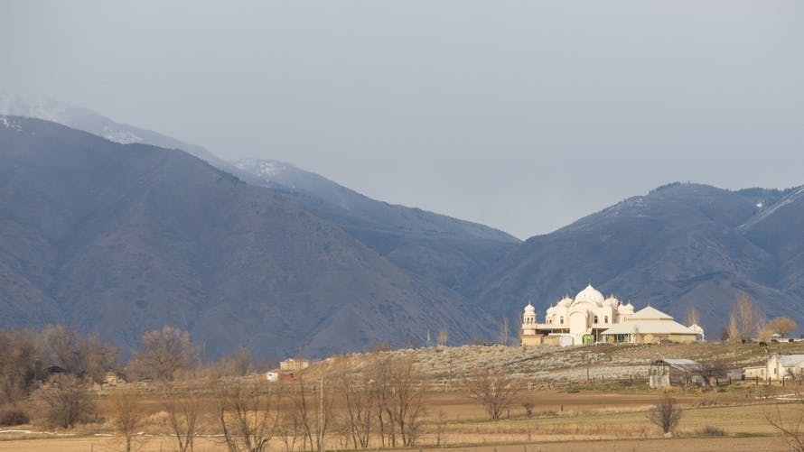 Free stock photo of hari krishna temple on hill below mountains clouds