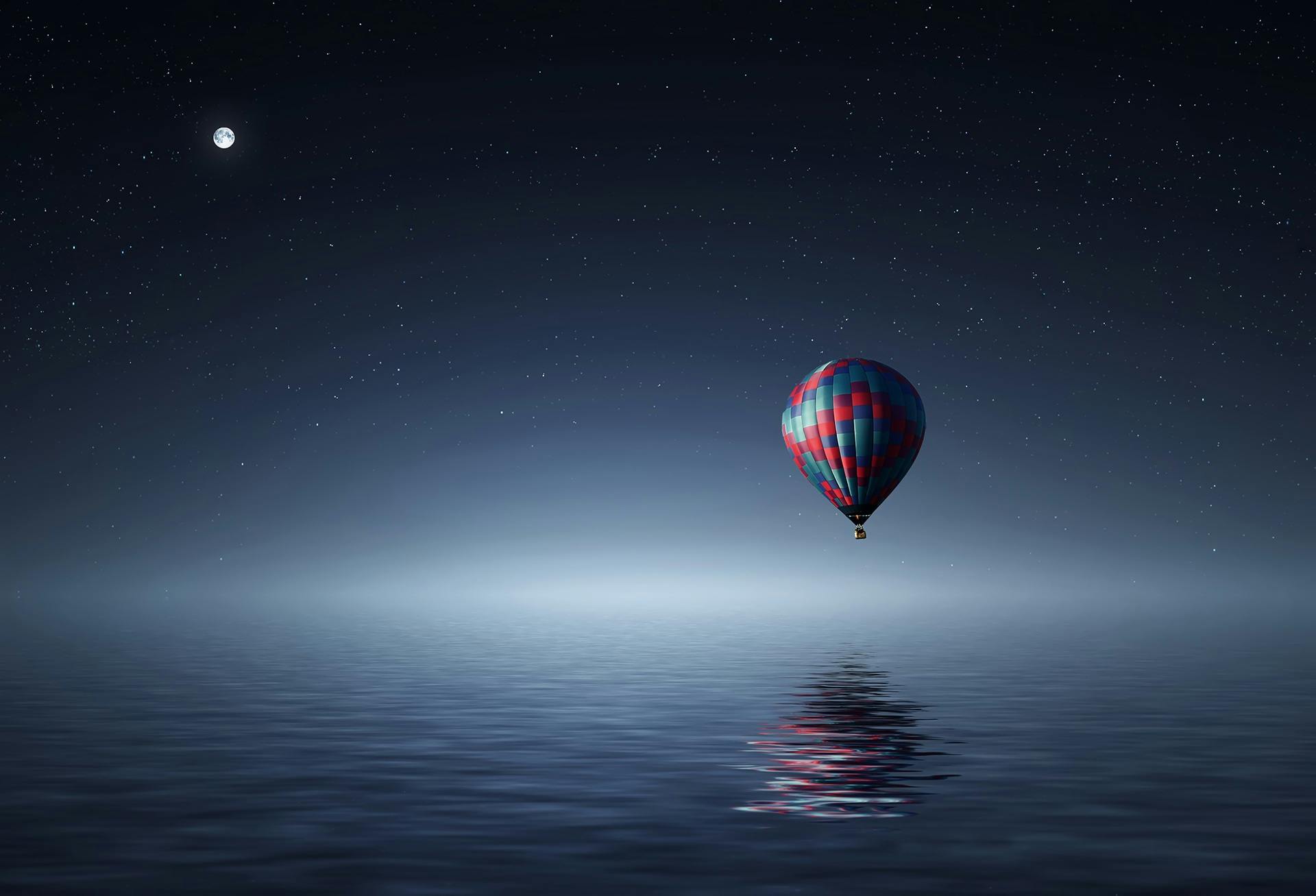 Wallpaper Red and Blue Hot Air Balloon Floating on Air on Body of Water during Night Time
