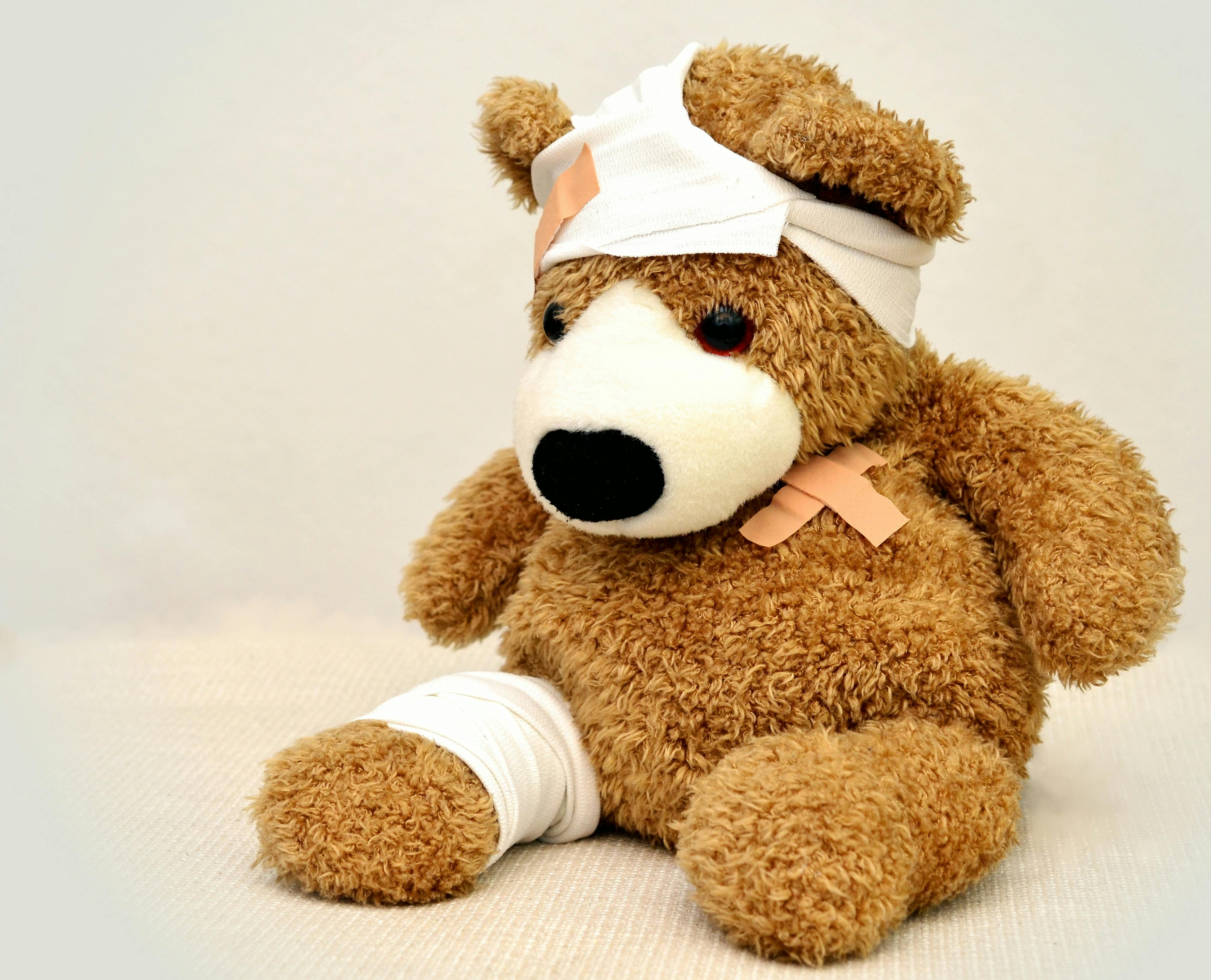Teddy bear with bandages on its leg, head, and chest.