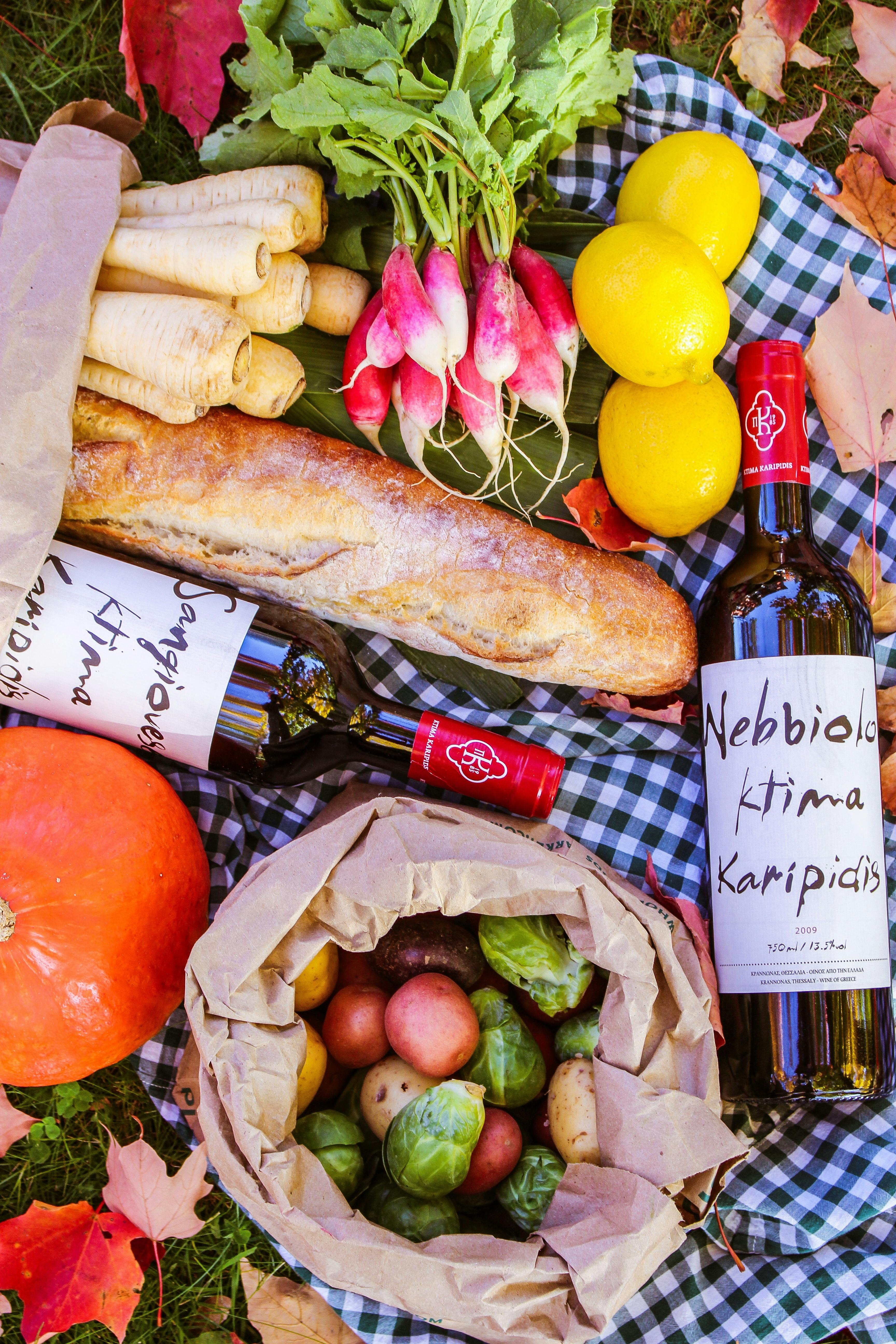 Fruit, vegetables, bread and wine laid out on a picnic blanket