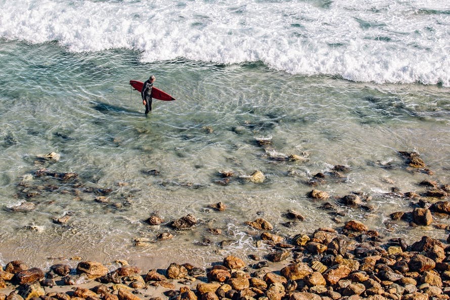 Person Holding Red Surfing Board in Clear Water Near Brown Stone during Daytime