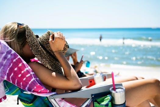 Woman Holding Brown Hat Sitting on Lounger in the Seashore at Daytime