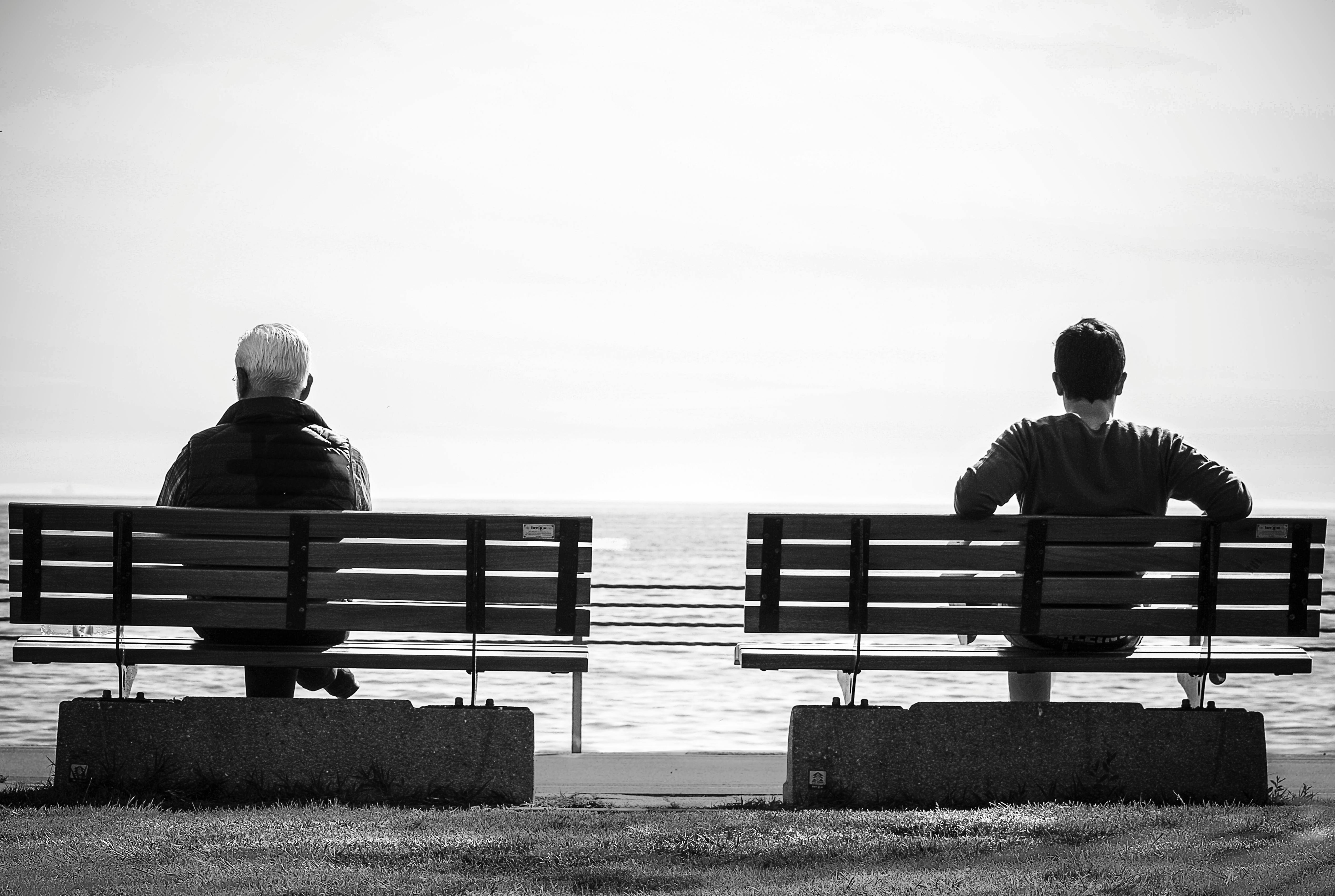 Black and white image of two men sitting on separate benches
